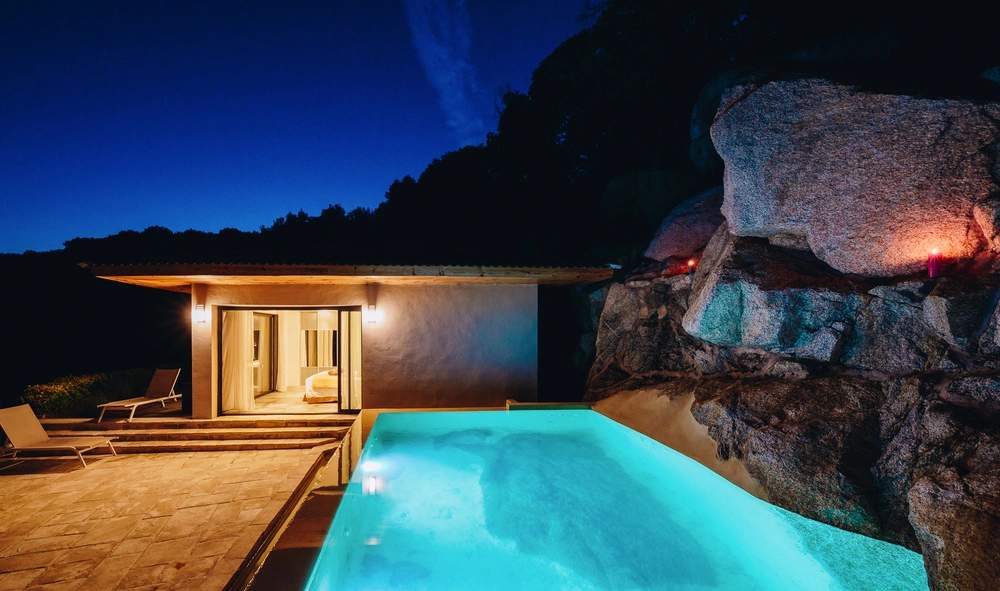 Résidence de luxe moderne avec piscine illuminée et rochers naturels en soirée