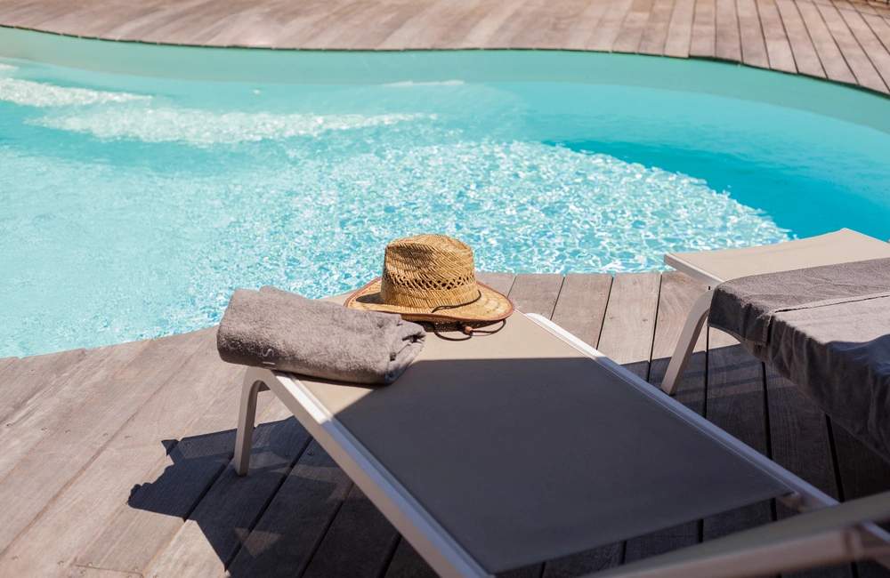 Résidence de luxe avec piscine turquoise, transat et chapeau de paille sur terrasse en bois