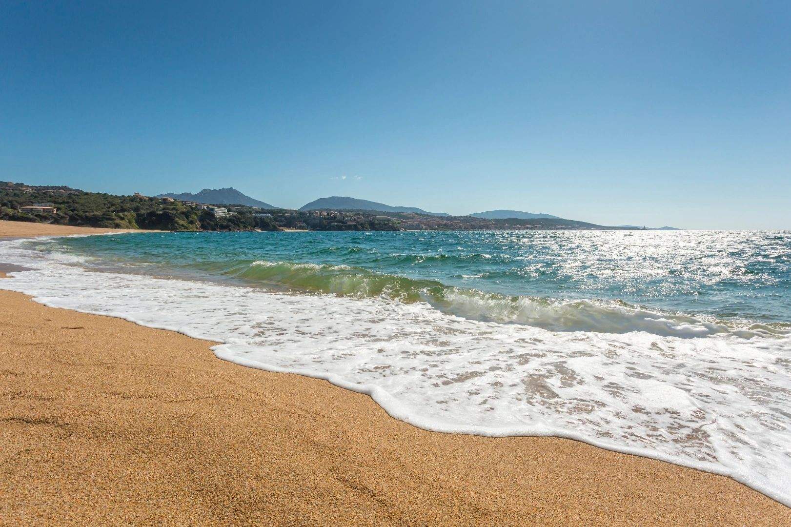 Plage de sable fin à Propriano avec vagues turquoise et montagnes en arrière-plan